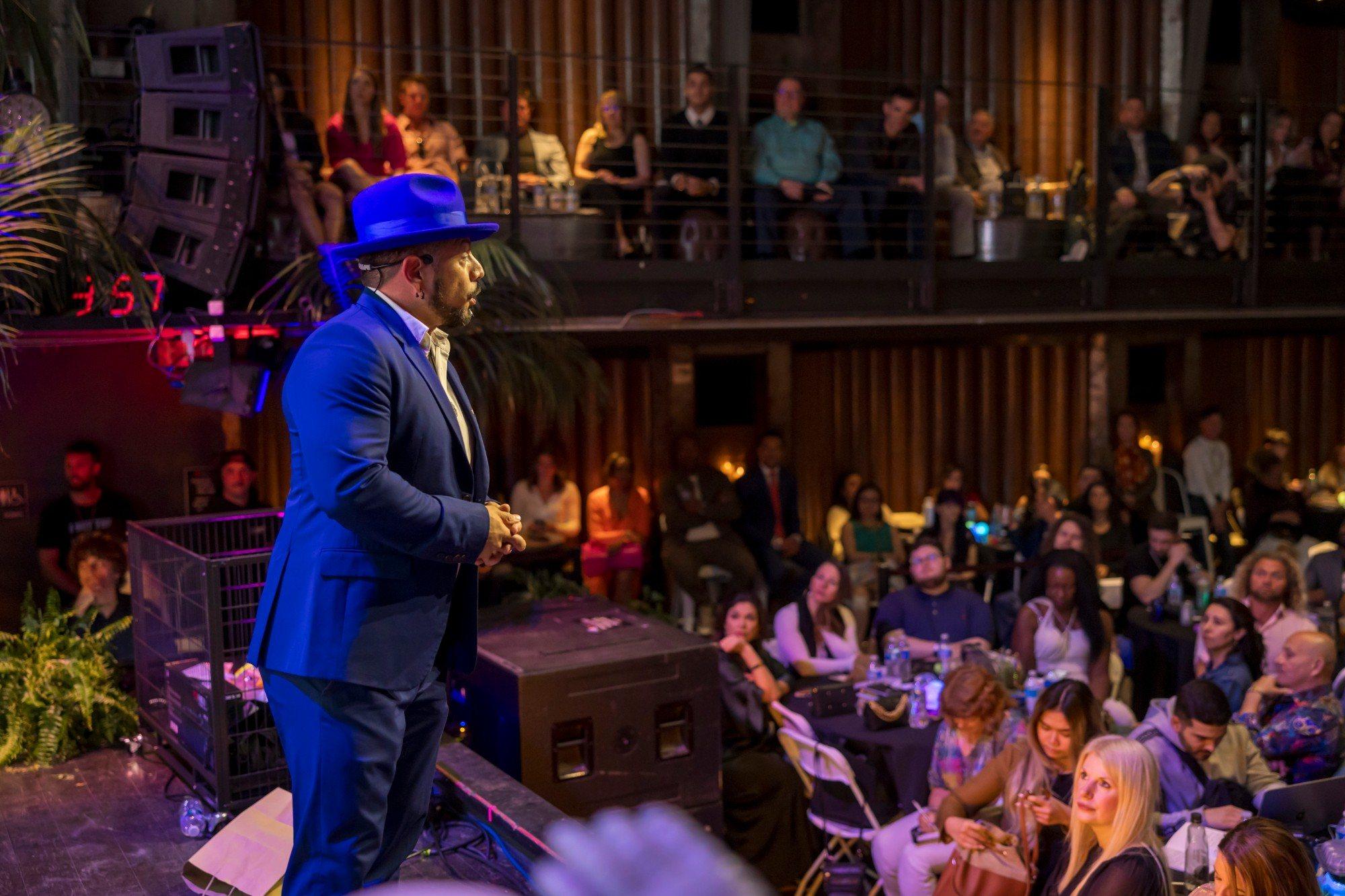 J.J. Villar in a blue hat speaking to a full room from the stage