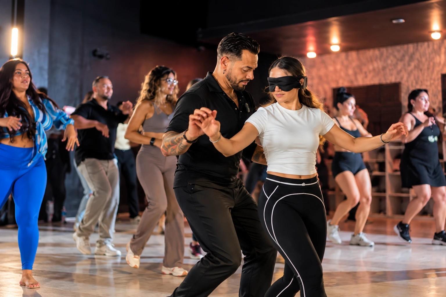 J.J. Villar partnering a blindfolded dancer through a movement exercise in a full studio