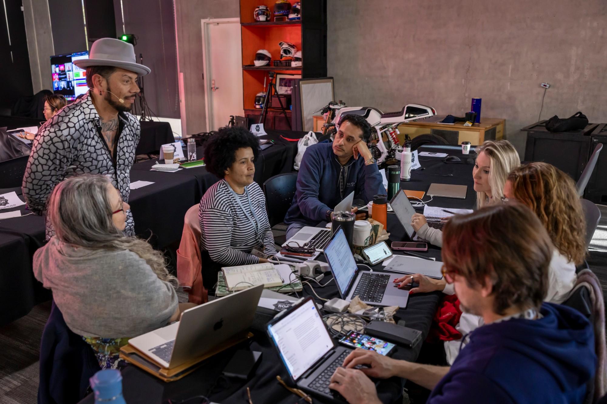 J.J. Villar standing over a team at their laptops, coaching them through a working session