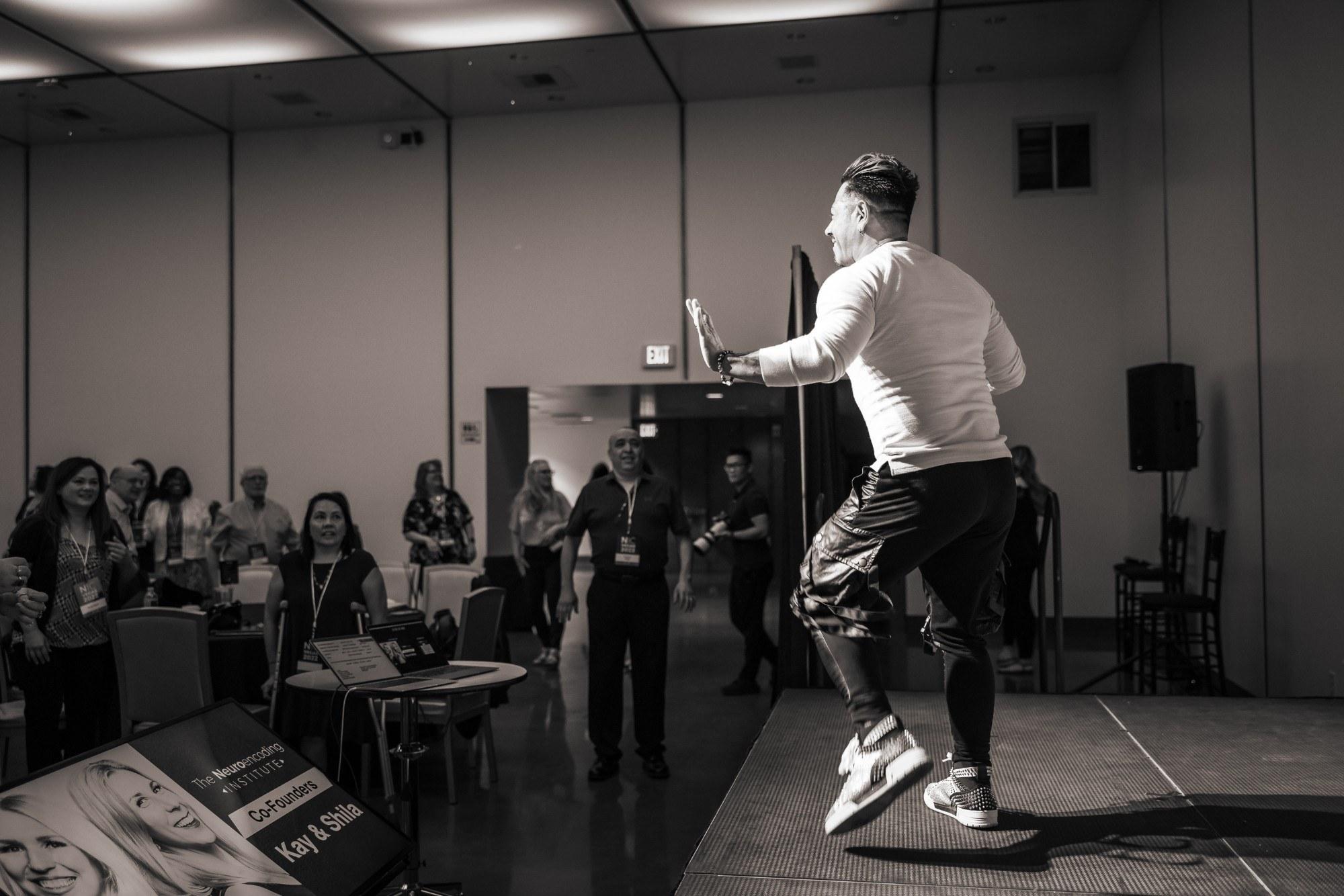 J.J. Villar leaping on stage in black and white as the audience stands and moves with him