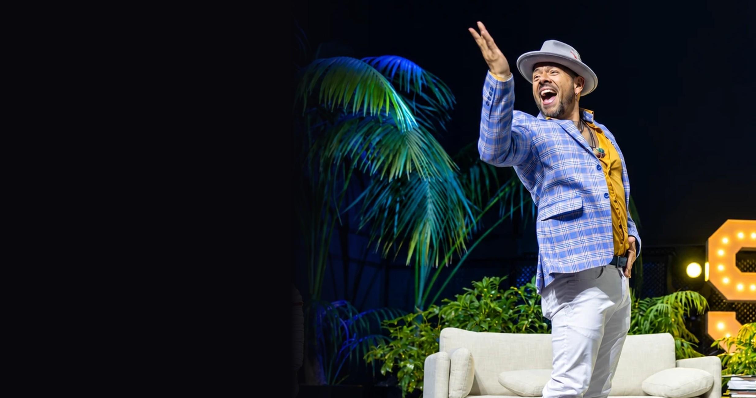 J.J. Villar on stage in a plaid blazer and hat, arm raised, mid-performance