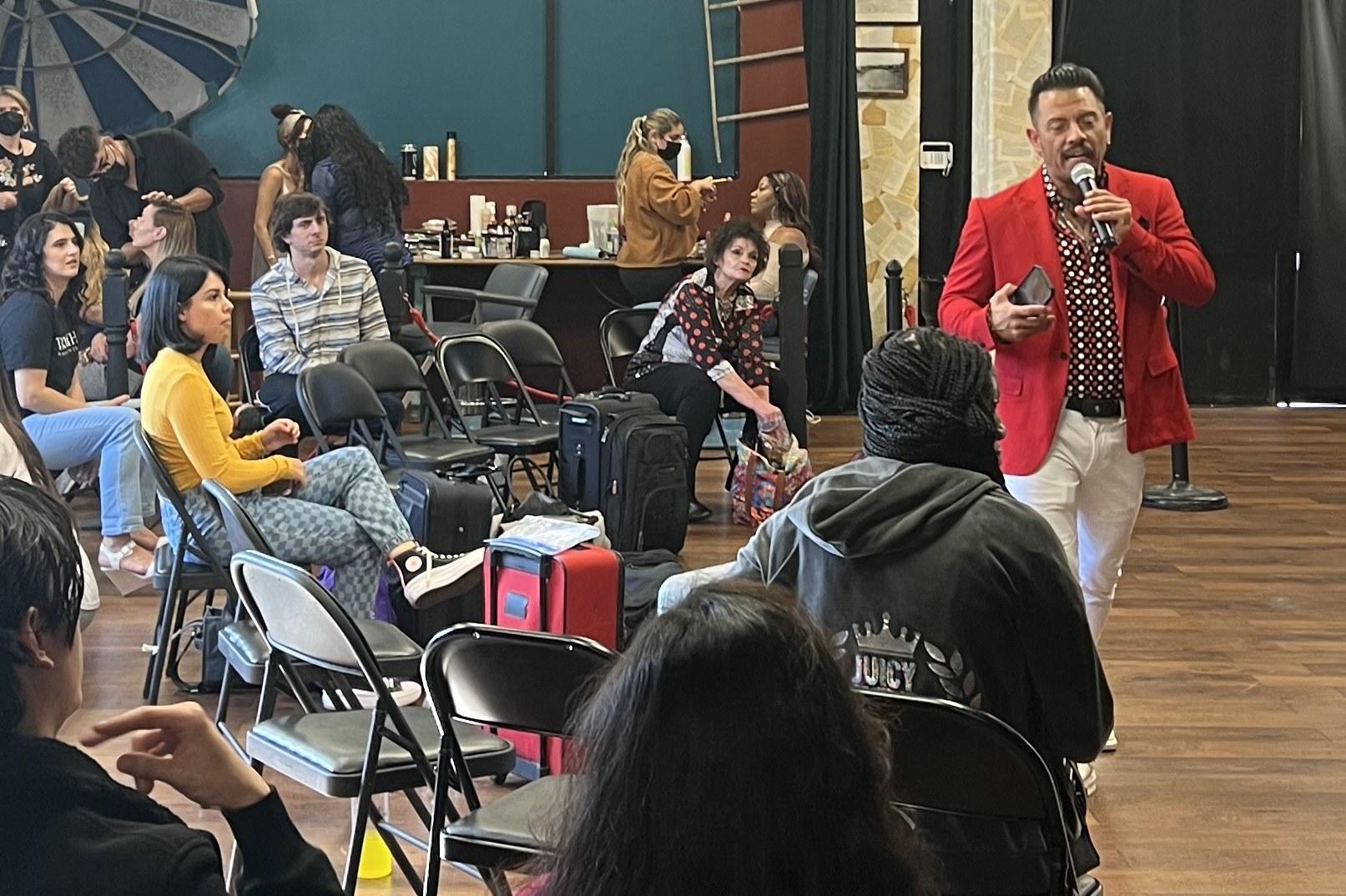 J.J. Villar in a red jacket speaking into a microphone to a room of seated participants